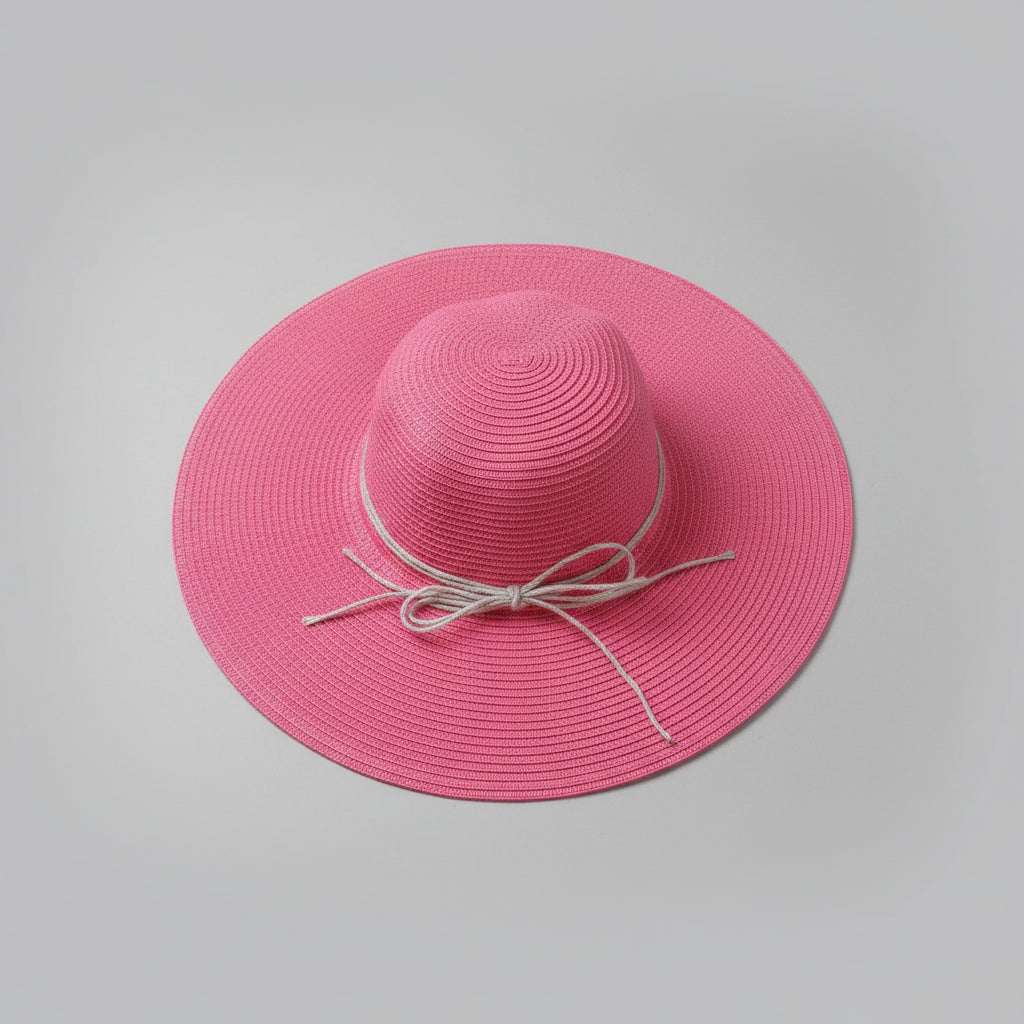 A pink woven sun hat with a wide brim and a light beige ribbon bow, displayed on a cardboard box.