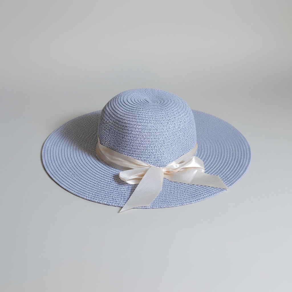 A light blue woven sun hat with a cream satin ribbon bow, resting on a brown cardboard box.