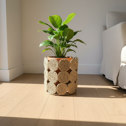 Seagrass rope-rosette basket used as a plant pot cover on a pale oak floor in a sunlit living room — Khoos
