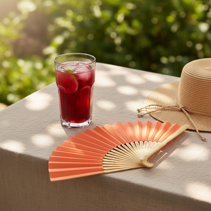 An orange folding hand fan with a light natural wood frame, shown partially open against a solid light gray background.