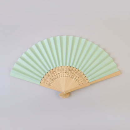 A traditional folding hand fan with pale mint green paper ribs and a natural light wood frame, shown partially open against a neutral light gray background.