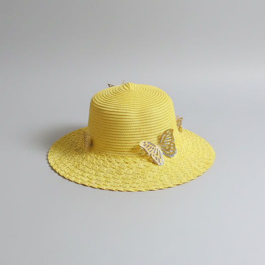 A yellow woven straw hat with a decorative white butterfly ornament on the brim, resting on a brown cardboard box.