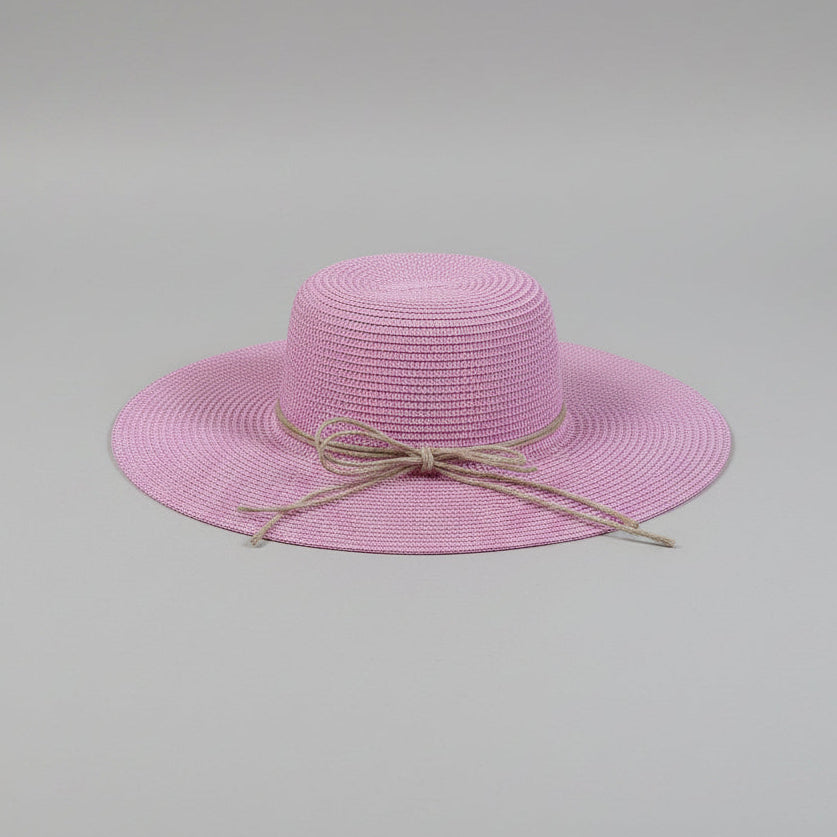 A light pink woven sun hat with a wide brim and a white bow, resting on a brown cardboard box.