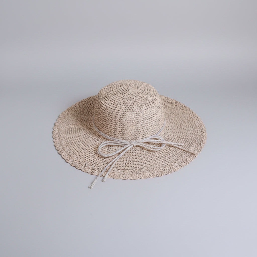 A light beige woven sun hat with a wide brim and a matching ribbon bow, resting on a brown cardboard box.