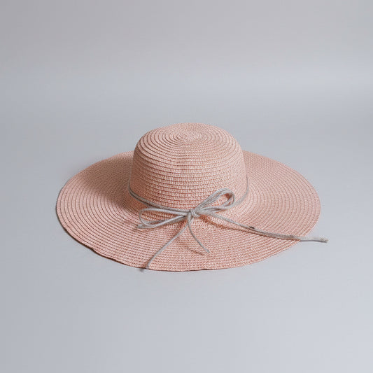 A light pink woven straw sun hat with a wide brim and a gray ribbon bow, resting on a cardboard box.