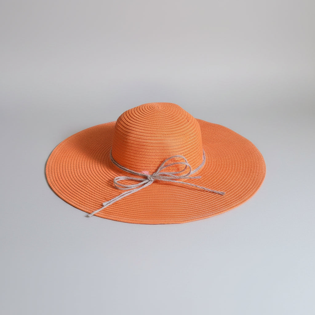 An orange woven sun hat with a wide brim and a light gray ribbon bow, resting on a brown cardboard box.