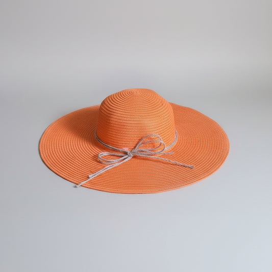 An orange woven sun hat with a wide brim and a light gray ribbon bow, resting on a brown cardboard box.
