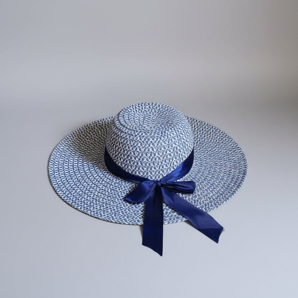 A woven sun hat with a blue and white pattern and a navy blue ribbon bow, resting on a brown cardboard box.