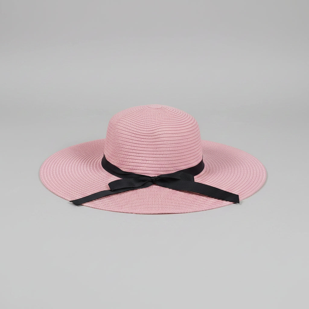 A pink woven sun hat with a black ribbon bow, displayed on a brown cardboard box.