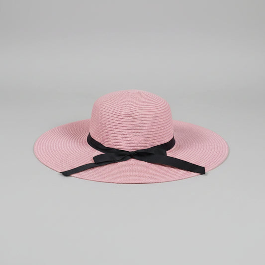 A pink woven sun hat with a black ribbon bow, displayed on a brown cardboard box.