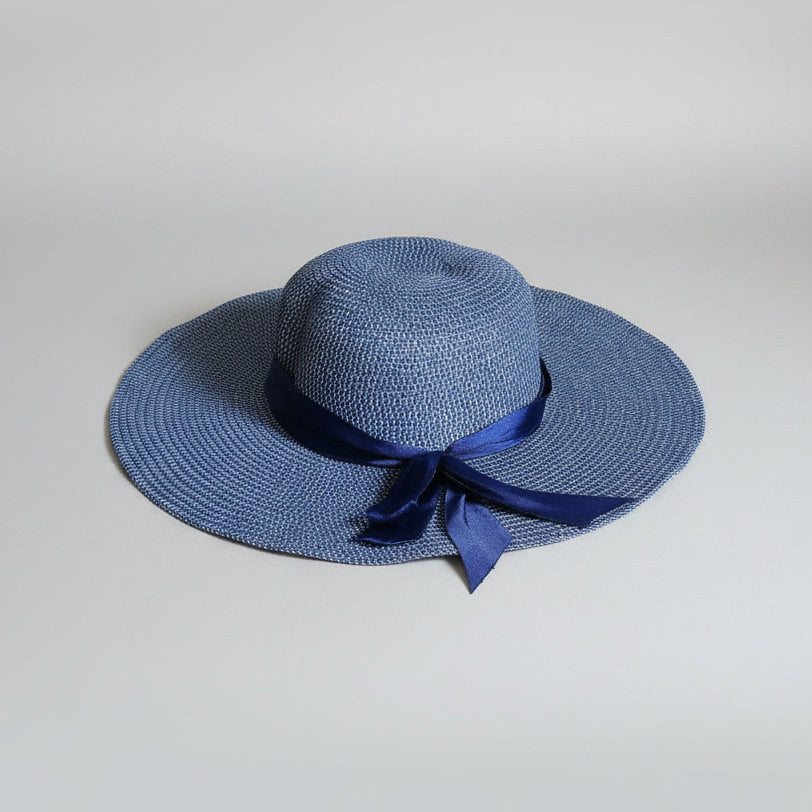 A blue woven sun hat with a navy blue ribbon bow, resting on a brown cardboard box.