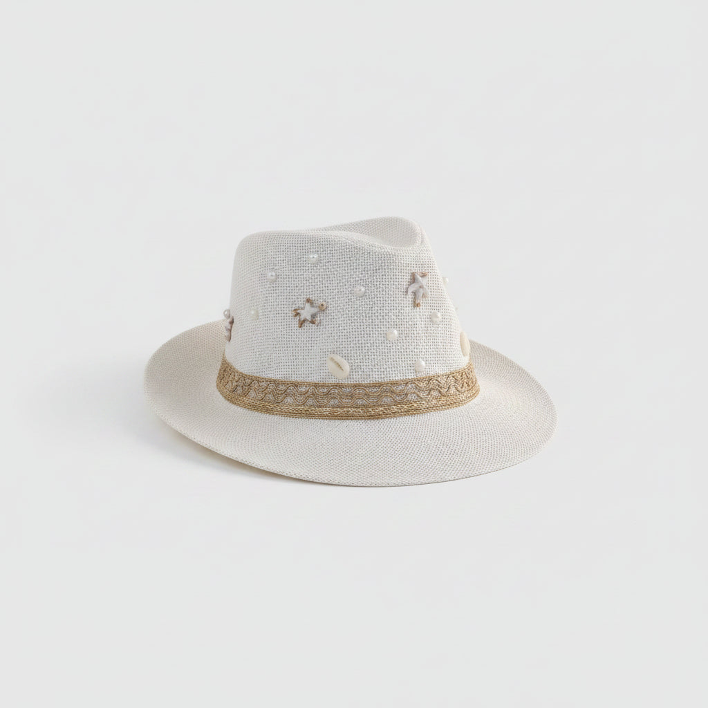 A white woven fedora hat with pearl-like embellishments and a tan band, displayed on a light gray shelf in a home setting.