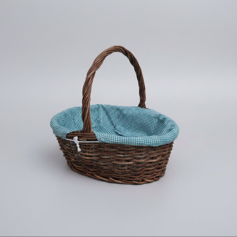 A brown woven basket with a twisted handle and a light blue and white gingham fabric lining, placed on a beige stone-tiled floor.