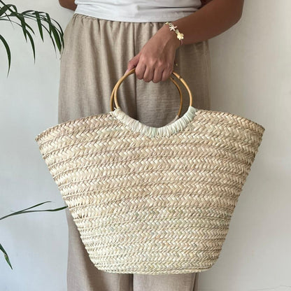 Woman walking barefoot along the shoreline carrying the Boho Breeze basket by its bamboo handles — Khoos