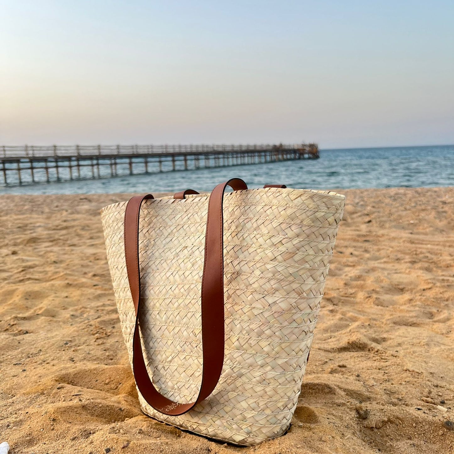 Palm beach bag with leather straps standing on a wooden pier with the sea behind — Khoos