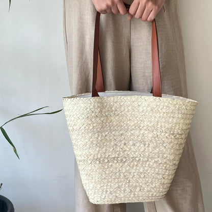 Palm beach bag with leather straps carried at the shoulder in pale linen clothing — Khoos