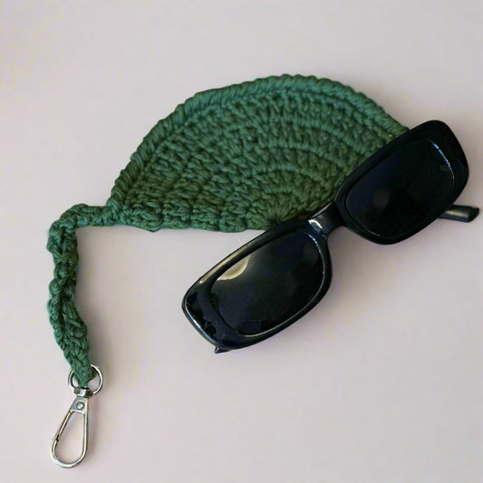 Olive hand-crocheted sunglasses case with a pair of black sunglasses tucked inside — Khoos