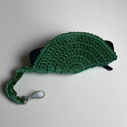 Olive hand-crocheted cotton sunglasses case seen from the side, showing the shell shape and strap — Khoos