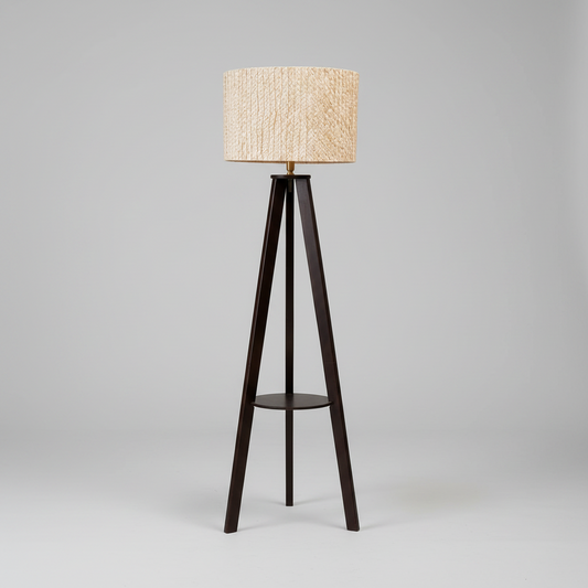 A tripod floor lamp with a dark brown wooden frame and a textured beige woven shade, standing on a dark marble floor against a white paneled wall.