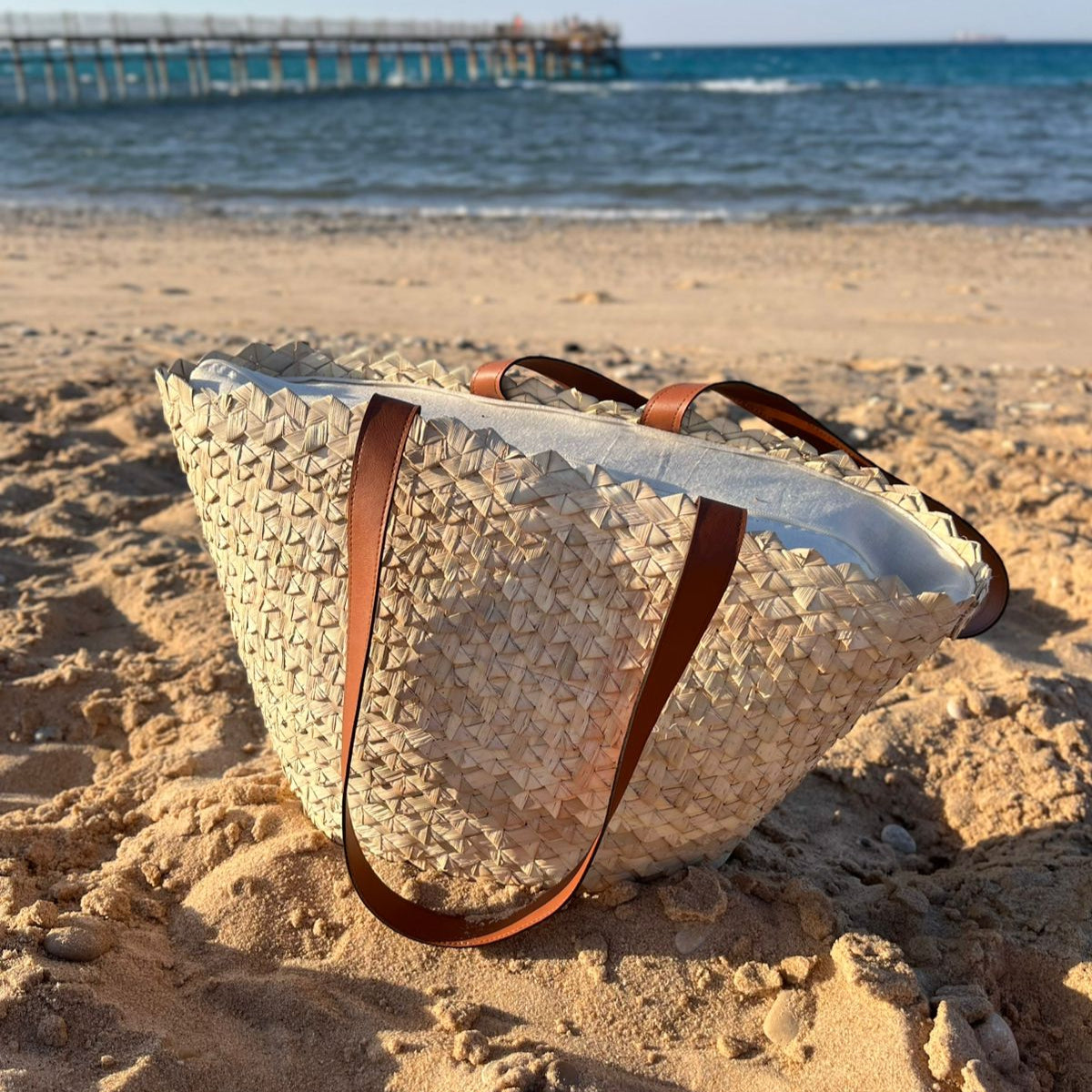 Eco-Chic palm tote standing on the sand at the shoreline — Khoos