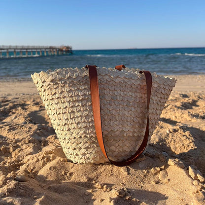 Eco-Chic palm tote on the beach seen from a low angle, sea behind — Khoos