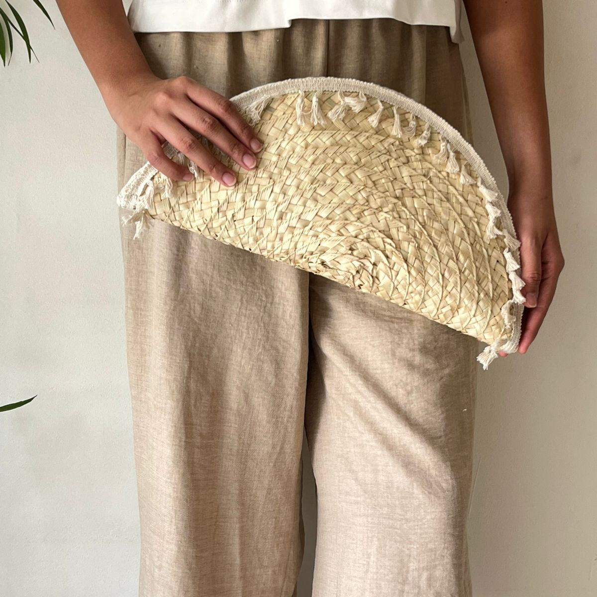 Fringed half-moon clutch held flat at the hip by a woman in a neutral cream outfit, showing scale — Khoos