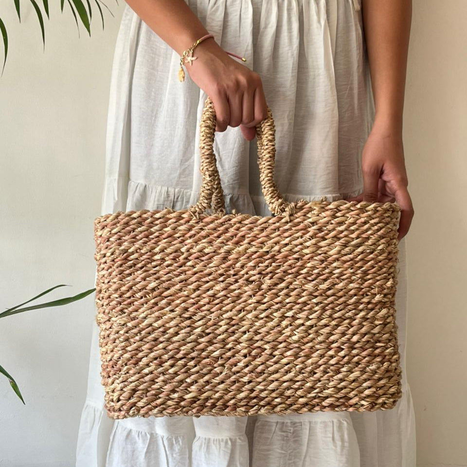 Halfa rectangular bag carried in the hand against a cream outfit, showing how it hangs when held — Khoos