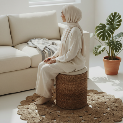 Woman seated on the Halfa Rolled Comfort Stool beside a sofa in a sunlit Cairo living room, showing it in use as seating — Khoos