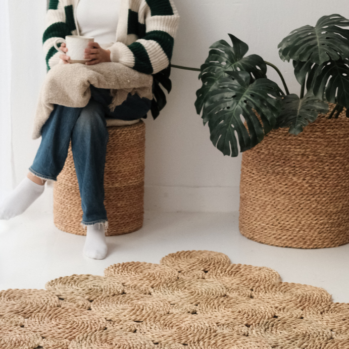 Person seated on the Halfa Rolled Comfort Stool beside a monstera plant, showing it in use as seating — Khoos