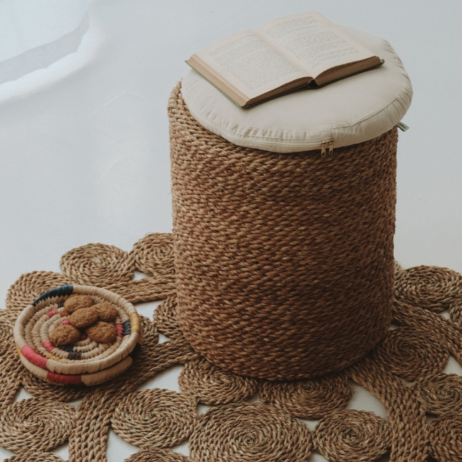 Halfa Rolled Comfort Stool with its cushion, styled on a woven rug with a book and a bowl of dates — Khoos