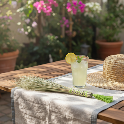 Lemonada manasha palm broom with green-and-white gingham handle and green tassel on a cream linen tablecloth in a sunlit garden, beside a tall glass of chilled lemonada with mint and a slice of lemon — Khoos