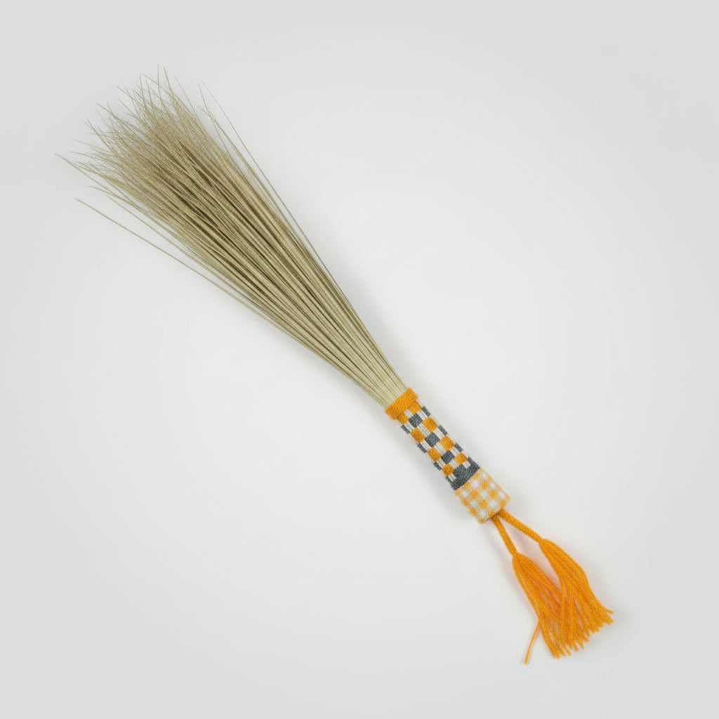 Yostafandi manasha palm hand broom with gold-and-black gingham handle and bright orange tassel, on a plain studio backdrop — Khoos