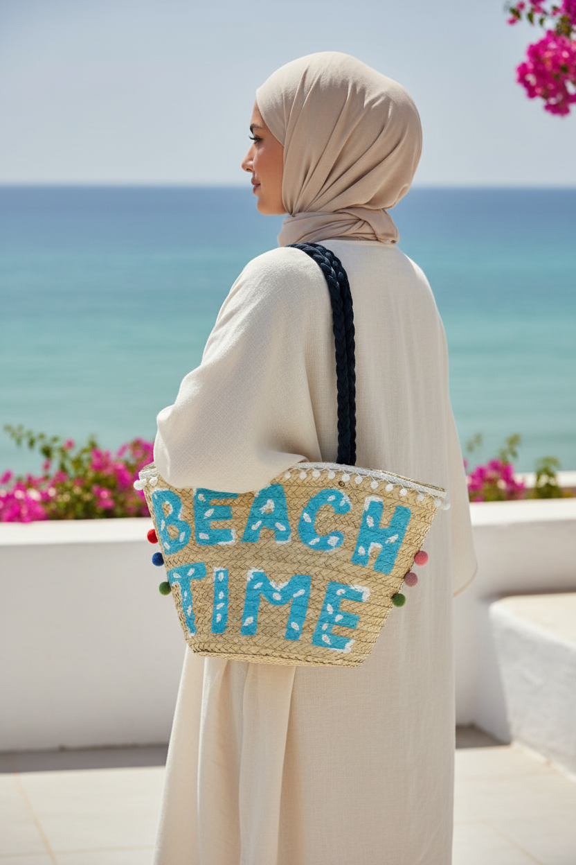 Woman carrying the palm leaf Beach Time tote with navy handles over her shoulder on a whitewashed North Coast terrace by the sea — Khoos