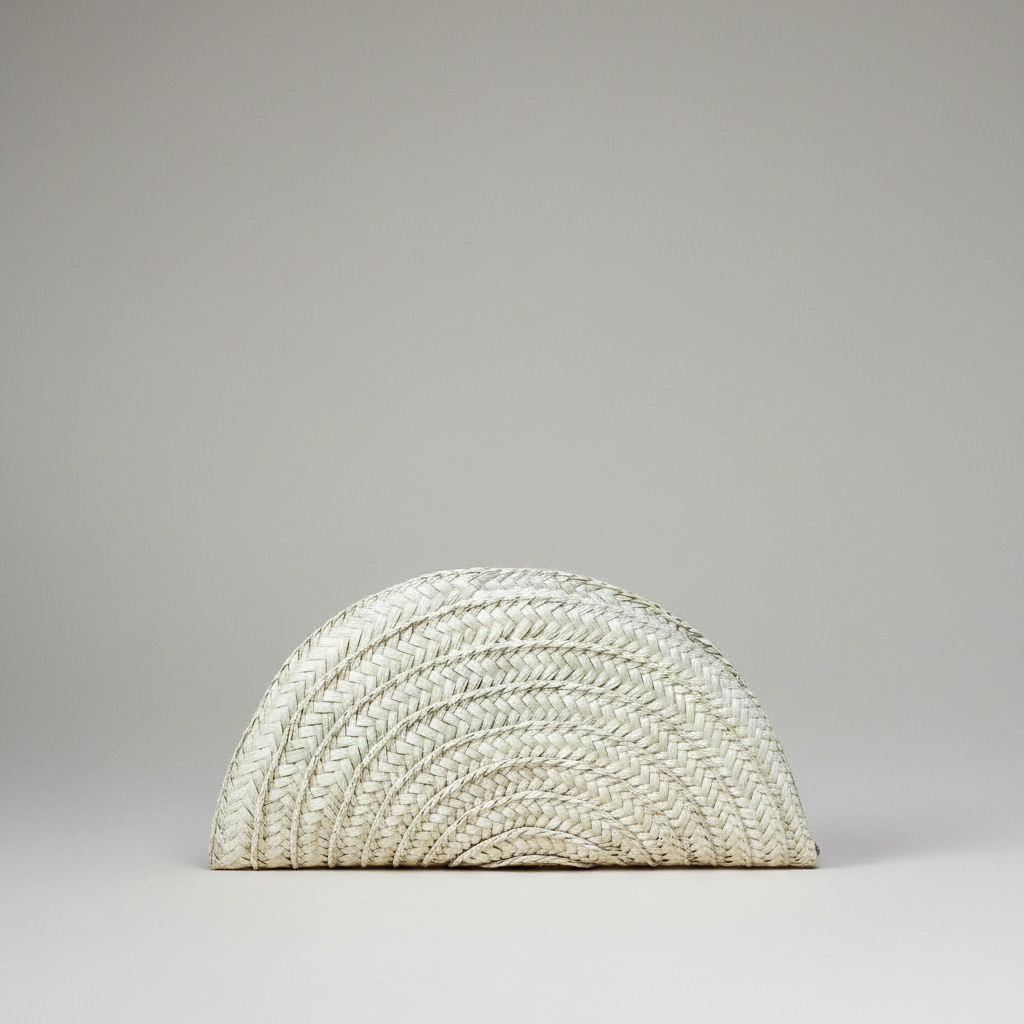 Handwoven palm leaf seashell half moon clutch in cream, shown alone on a grey studio backdrop — Khoos