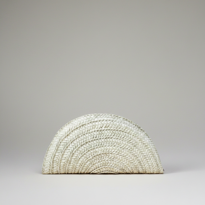 Handwoven palm leaf seashell half moon clutch in cream, shown alone on a grey studio backdrop — Khoos
