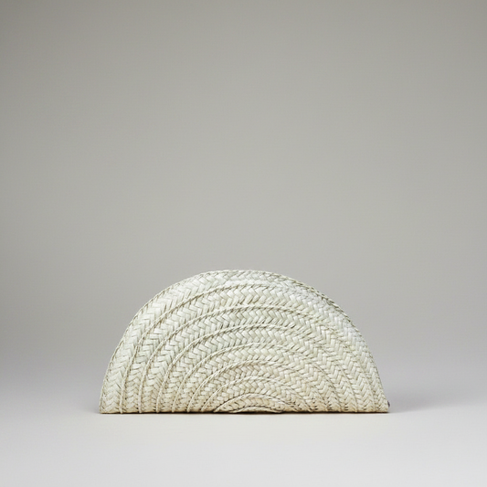 Handwoven palm leaf seashell half moon clutch in cream, shown alone on a grey studio backdrop — Khoos