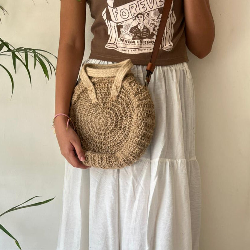Round jute crossbody bag with leather strap worn across the body over white summer clothing — Khoos