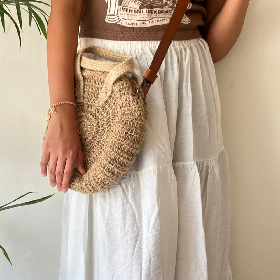 Round jute crossbody bag worn at the hip, showing the leather strap across the body — Khoos